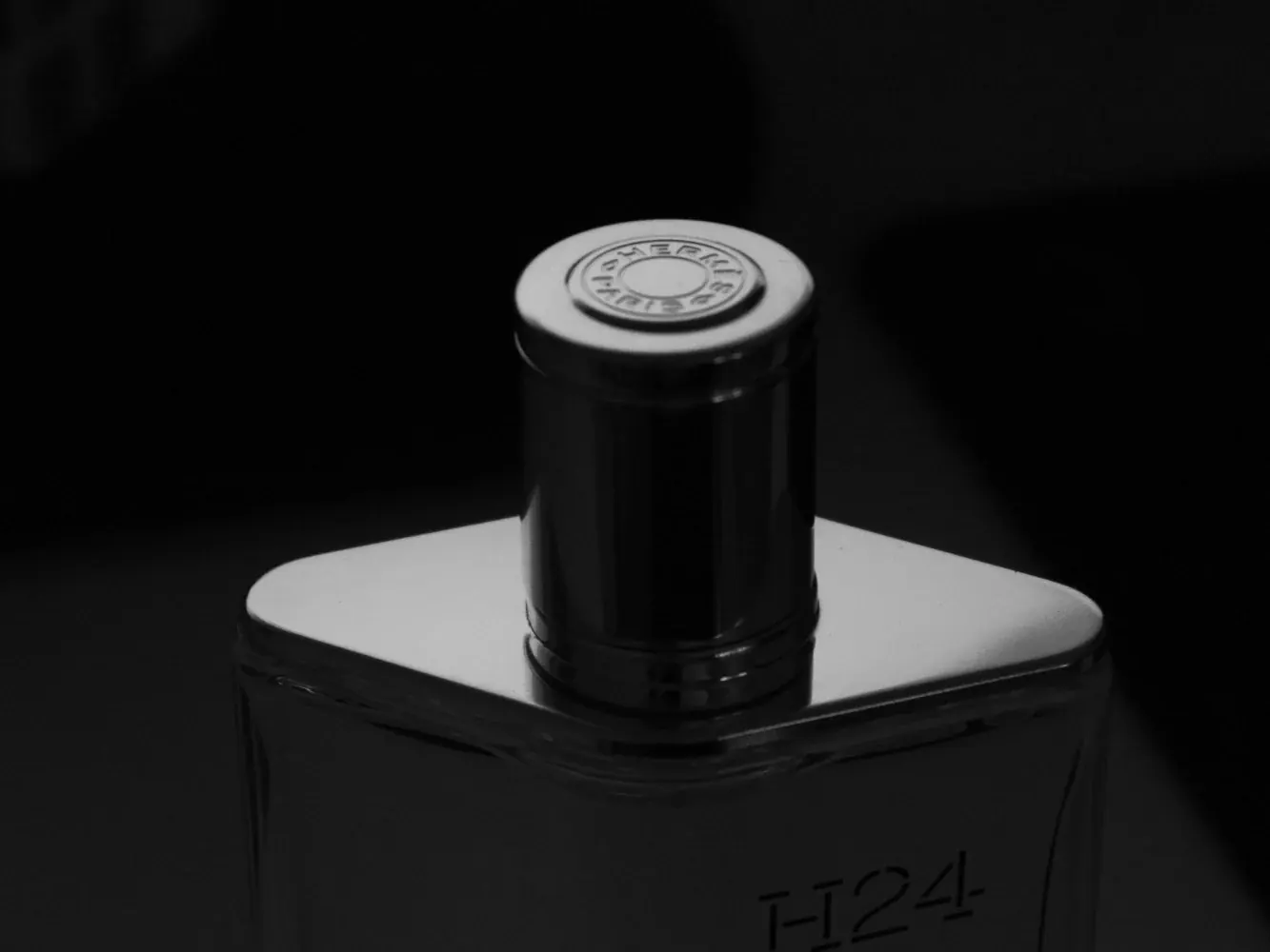 Black-and-white close-up of a glass perfume bottle with a silver cap