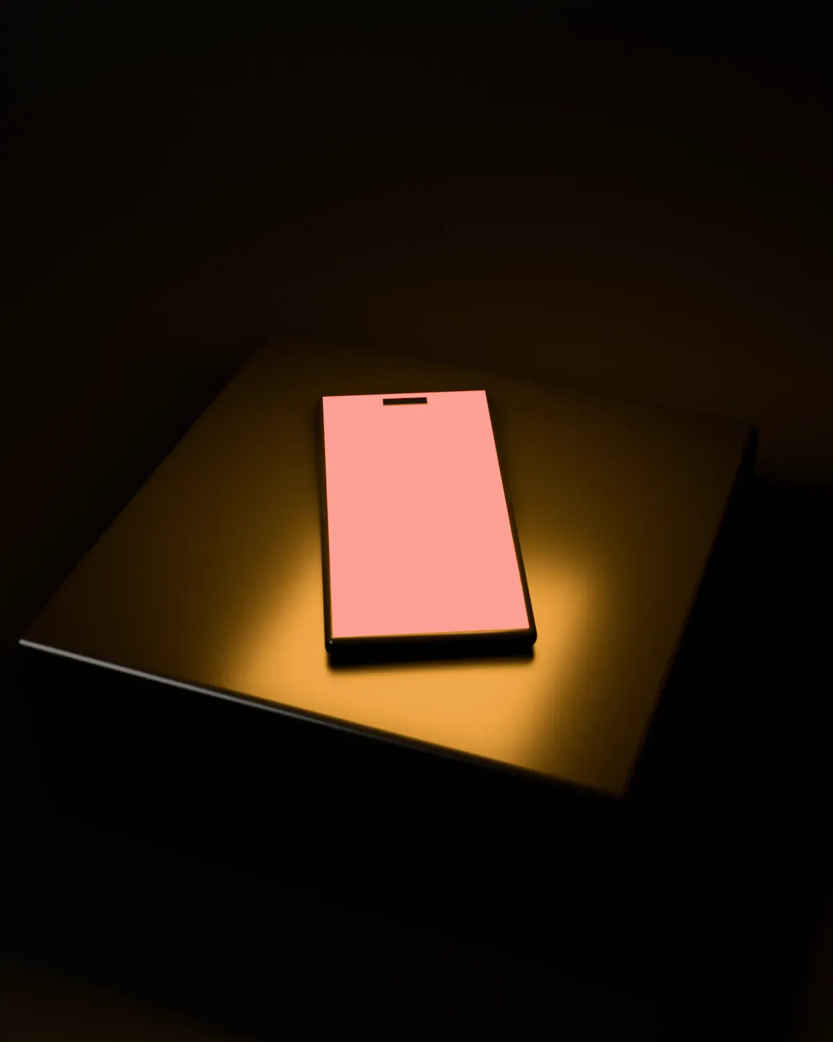 A Lumen phone lying face up on a black block, light spilling onto it